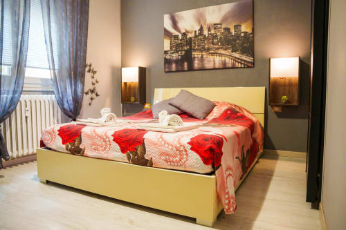 Modern bedroom at Navigli Affittacamere in Rozzano with yellow bed frame, red patterned bedding, city view artwork, and warm