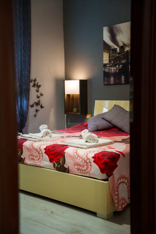 Modern bedroom in Casa Linda Rozzano with red rose bedding, yellow bed frame, city view photo, ambient lighting, and rolled