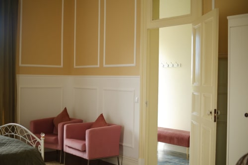 Villa Várzea bedroom with cream and gold walls, red armchairs, and cream paneled doors opening to terrace, Portugal B&B