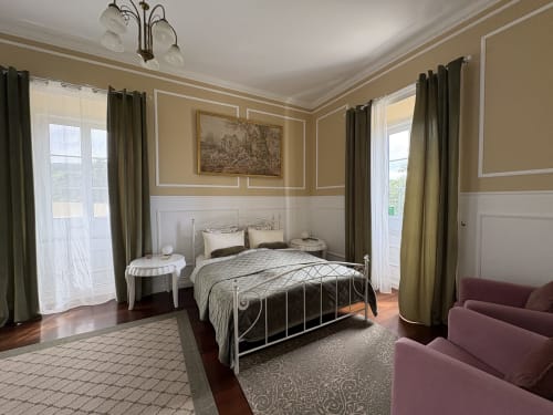 Elegant bedroom at Villa Várzea B&B with ornate iron bed, cream and gold walls, arched windows, and burgundy seating in