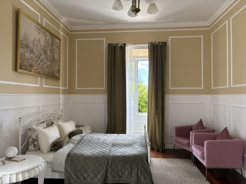 Elegant bedroom at Villa Várzea with beige and white décor, metal bed frame, green accents, and garden views through doors