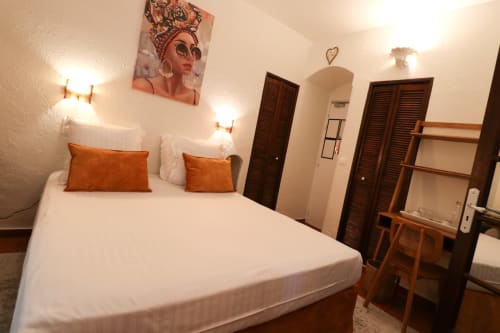Queen bed with orange pillows in Hotel Villa Roseraie room, Vence, featuring white bedding and warm lighting