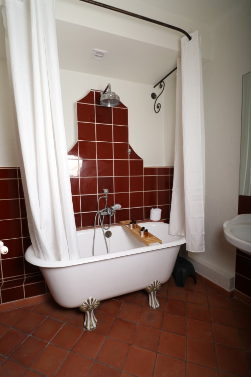 Baignoire ancienne sur pieds avec carrelage rouge et rideau de douche blanc dans la salle de bains de l'Hôtel Villa Roseraie, Vence