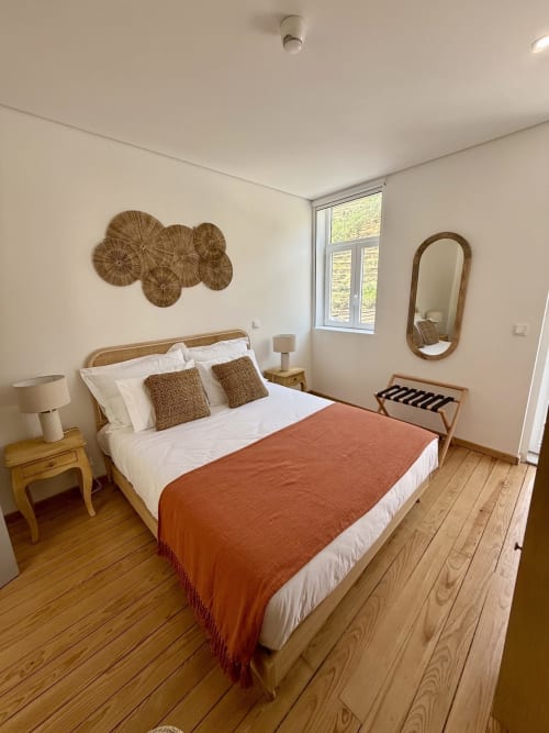 Bright bedroom with rattan-framed bed, orange throw, wooden floors, and wall baskets at Casa Tawny in Pinhão
