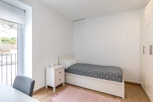 Bright single bedroom at Residencia Demar in Godella with bed, nightstand, balcony access, and wooden flooring.