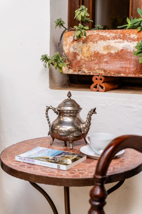 Mesita rústica en La Vista Medina Stays con tetera de latón, libro y suculentas en maceta en rincón de ventana