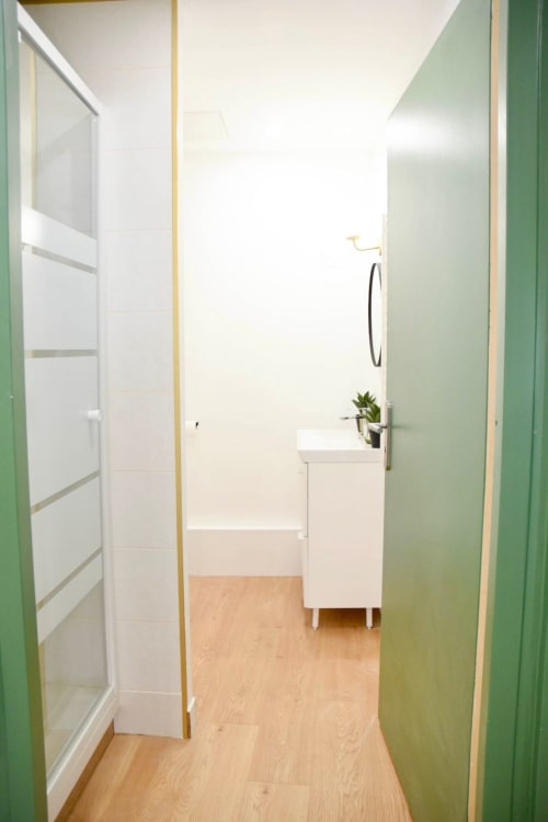Modern bathroom in Wellkhome Bordeaux apartment with white sink, green walls, wooden floor and shower