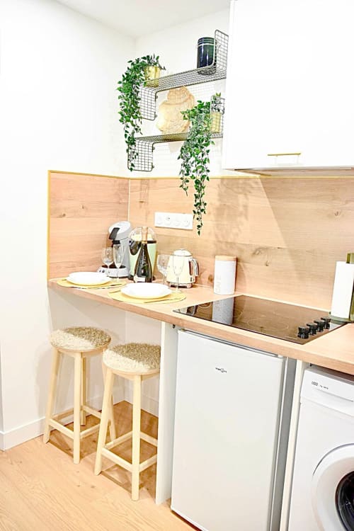 Modern kitchenette at Wellkhome Bordeaux with wooden counter, bar seating, appliances, and cascading plants on wire shelving
