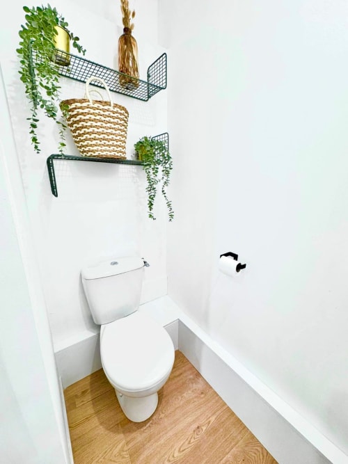 Modern bathroom at Wellkhome Bordeaux with toilet, wooden flooring, white walls, and hanging plants on wall-mounted shelves