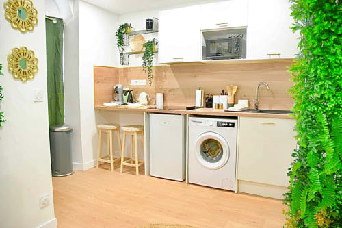 Modern kitchen in Wellkhome Bordeaux apartment with washing machine, wooden counters, green plants, and gold accents