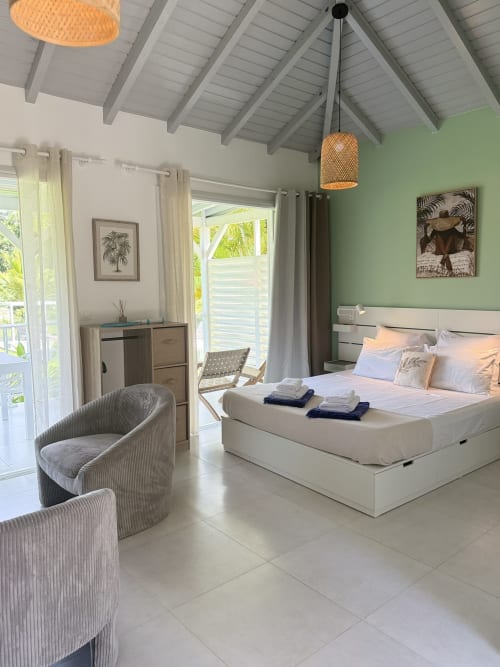 Bright modern bedroom at Domaine de la Glacière with white bed, mint green walls, woven pendant light, and tropical views in