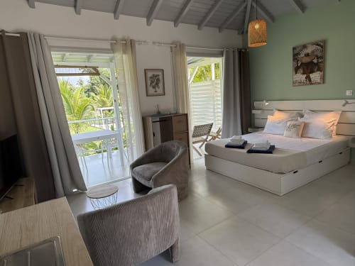 Bungalow Héliconia à Domaine de la Glacière, Petit Bourg : chambre spacieuse avec lit blanc, murs verts, accès au balcon