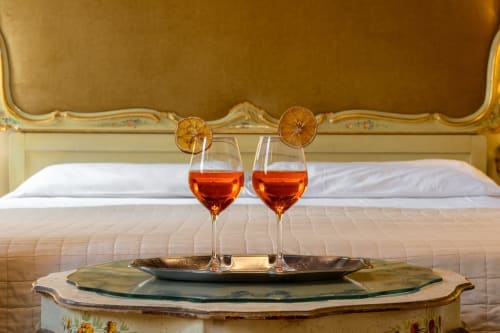 Deux verres d'apéritif avec des tranches d'orange séchée sur un lit luxueux dans une chambre d'hôtel vénitienne donnant sur le canal