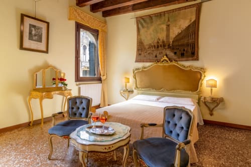Élégante chambre double vénitienne avec lit or orné, fauteuils bleu velours, vue sur le canal et décor classique au Palazzo San Firmino,