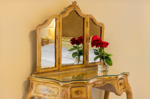 Miroir de toilette doré orné avec roses rouges dans un vase, reflétant un lit dans une chambre d'hôtel vénitienne