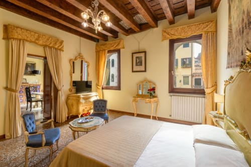 Chambre double vénitienne élégante avec vue sur canal, mobilier orné, poutres apparentes et fauteuils bleus au Palazzo San