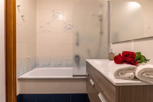 Salle de bain moderne d'un B&B vénitien avec baignoire, paroi de douche en verre, lavabo garni de serviettes et roses rouges