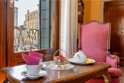 Élégant salon de la Suite Royale au Palazzo San Firmino à Venise avec fauteuils en velours rose, table en bois et vue sur le Grand Canal