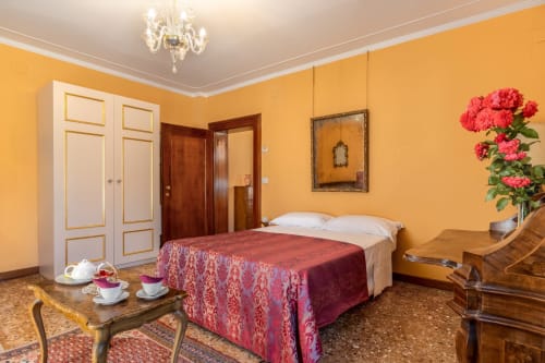 Suite Royale luxueuse au Palazzo San Firmino à Venise avec murs jaunes, lit orné, fleurs fraîches et mobilier élégant