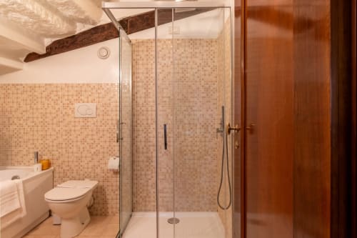 Salle de bain moderne dans un hôtel vénitien avec douche italienne, carrelage mosaïque beige, toilettes et porte en bois
