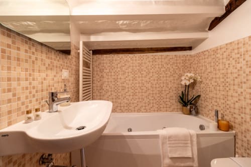 Salle de bain moderne de suite hôtelière vénitienne avec carrelage mosaïque pêche, lavabo blanc, baignoire et poutres en bois