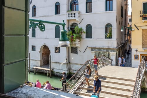 Vue d'un canal de Venise avec un palazzo historique, eau verte, pont orné et touristes sur la place ensoleillée du Palazzo San