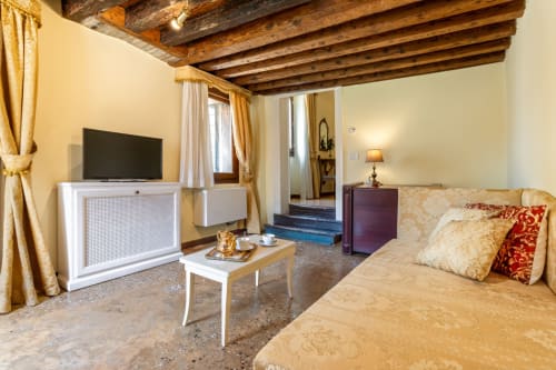 Suite junior élégante avec poutres apparentes, canapé, télévision et vue sur le canal au Palazzo San Firmano à Venise