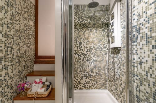 Salle de bains moderne aux murs en mosaïque tons terre, douche vitrée et étagère en bois avec articles de toilette au Palazzo San