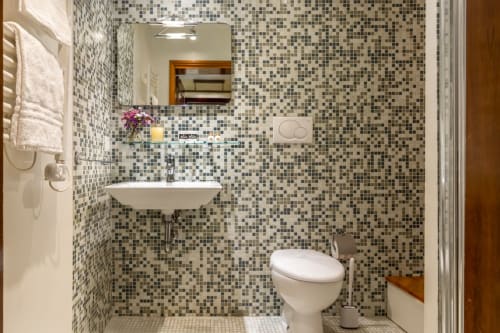 Salle de bain moderne à l'hôtel Venezia avec carrelage mosaïque, lavabo blanc, toilettes, miroir et porte-serviettes