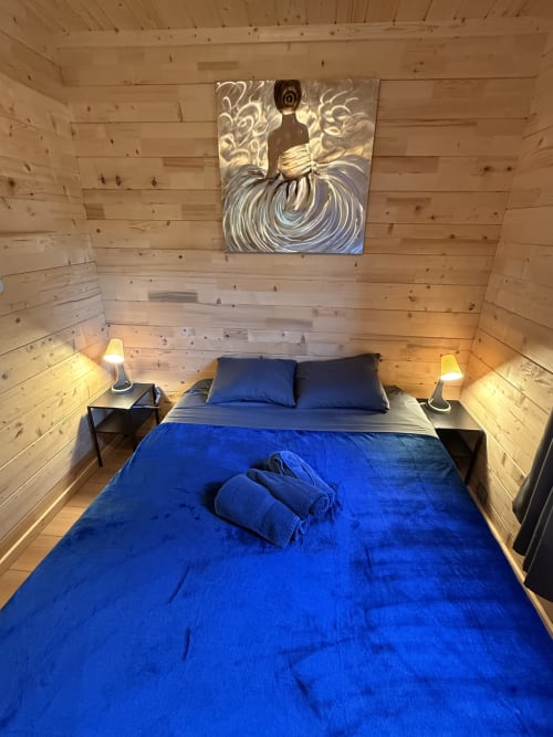 Accogliente camera da letto in legno con biancheria blu, due lampade e arte murale presso Cabanes et lodges du Belvédère