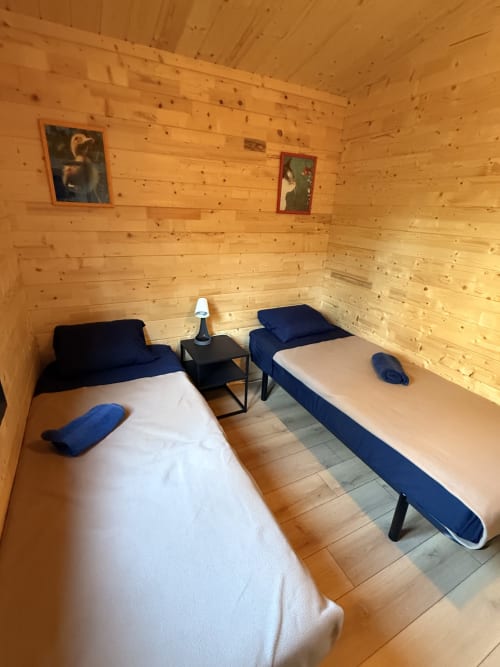 Camera twin in lodge in legno presso Cabanes du Belvédère con biancheria blu, tavolo centrale e arte incorniciata su pareti di pino