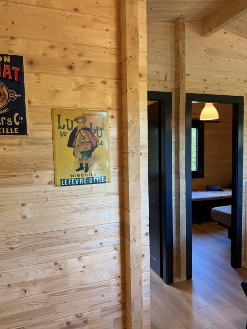 Corridoio interno di lodge in legno con poster vintage di biscotti francesi in cornice nera, porta che conduce a camera con vista sul lago