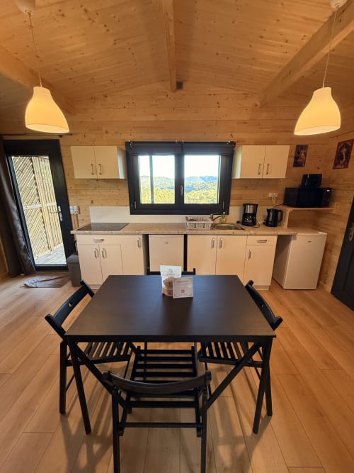 Sala da pranzo di lodge in legno con tavolo nero, cucina e vista sulle montagne alle Cabanes du Belvédère, Serrières-sur-Ain