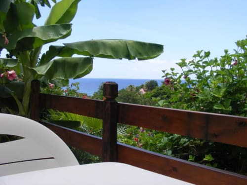 Vue océanique depuis la terrasse du Studio Citron Vert du Gîte Tainaco à Vieux-Habitants, Guadeloupe, avec jardin luxuriant et balustrade en bois