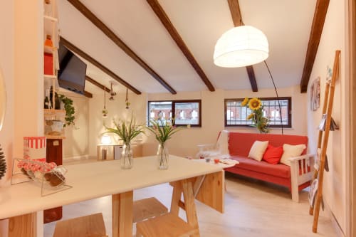Villa nórdica Buhardilla luminosa en Salamanca con vigas de madera, sofá rojo, mesa de comedor, plantas y techo expuesto