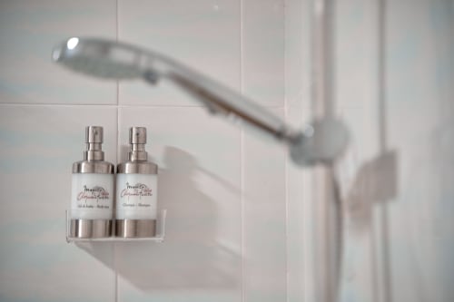 Dos botellas de spray blancas en organizador de ducha sobre pared de azulejos de baño con cabezal de ducha desenfocado arriba en MoneoHeritage Loft