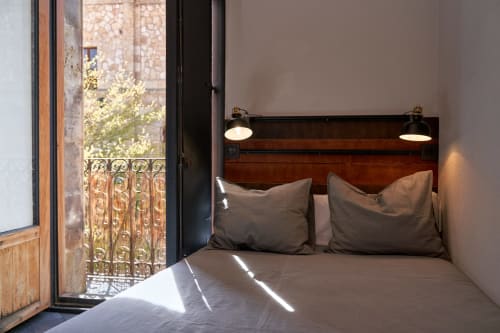 Dormitorio moderno en loft de Salamanca con cabecero de madera, ropa de cama gris, puerta balconera con vistas a la ciudad e iluminación ambiental
