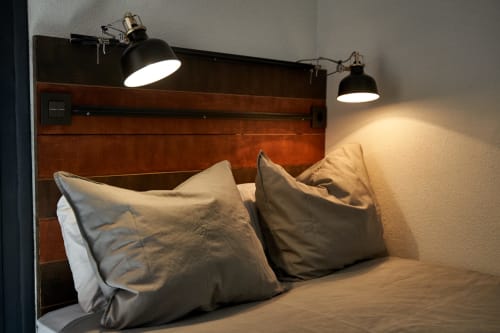 Dormitorio tipo loft industrial en hotel de Salamanca con cabecero de madera, dos almohadas grises y lámparas colgantes negras.