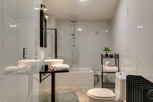 Baño moderno en loft de Salamanca con ducha de lluvia, lavamanos de cerámica, inodoro y detalles industriales en negro