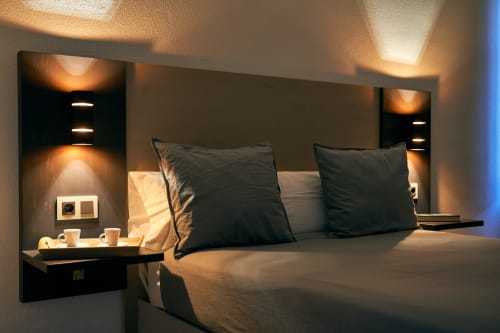 Habitación moderna en hotel de Salamanca con iluminación ambiental, almohadas negras, hornacinas junto a la cama con lámparas cálidas y servicio de café