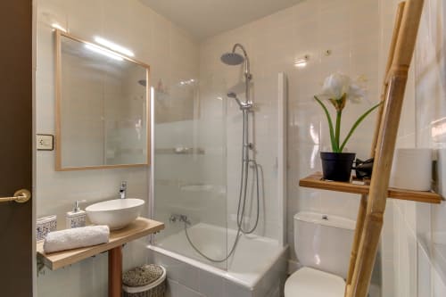 Baño moderno en hotel de Salamanca con ducha, lavabo blanco, inodoro, mueble de madera y decoración floral blanca
