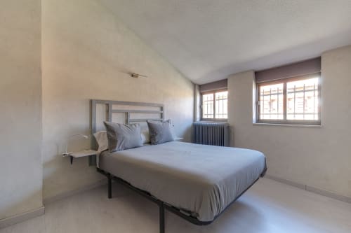 Dormitorio minimalista en la buhardilla del hotel MoneoHeritage de Salamanca con cama queen, almohadas azules, ventanas, radiador y diseño moderno