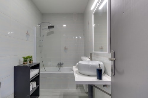 Baño moderno de la villa MoneoHeritage en Salamanca con lavabo redondo, ducha abierta, espejo LED y diseño minimalista