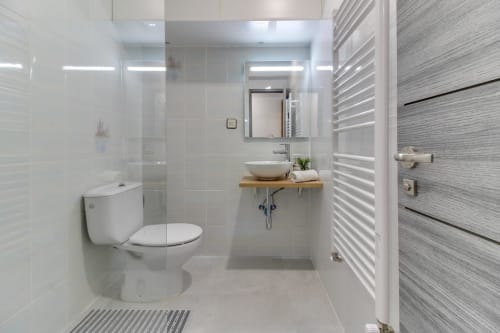 Baño moderno del hotel MoneoHeritage en Salamanca con ducha a ras de suelo, lavabo blanco, inodoro y toallero calefactable