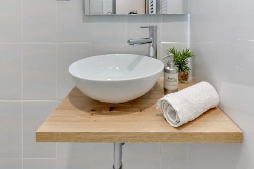 Elegante lavabo blanco sobre mueble de madera en el hotel MoneoHeritage de Salamanca, con toallas enrolladas y plantas decorativas