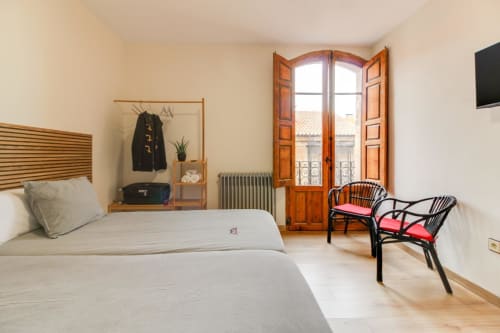 Luminosa habitación de hotel en Salamanca con cama, puertas de madera, radiador y sillas tapizadas en rojo junto a la ventana