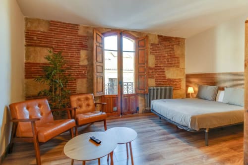 Apartamento Estudio San Pablo en el hotel MoneoHeritage de Salamanca con paredes de ladrillo, cama de madera, sillones de cuero y decoración francesa