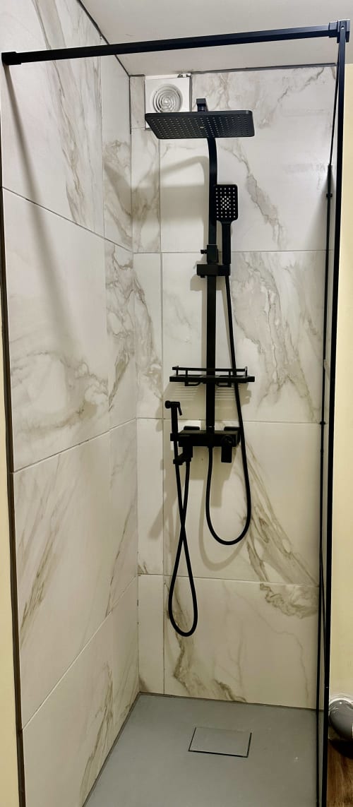 Nowoczesny czarny system prysznica deszczowego w łazience wyłożonej marmurową płytką w hotelu Ombre de la Tour, Lourdes