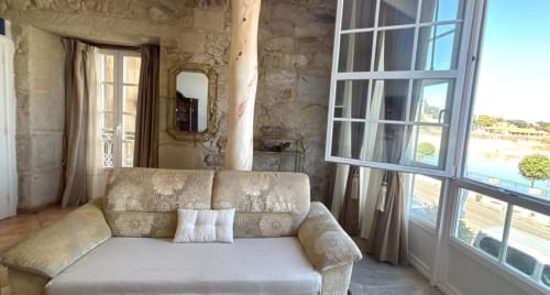 Sofá floral beige con vistas al mar desde balcón en apartamento boutique Solpor, Baiona. Paredes de piedra, espejo ornamentado, grandes ventanales