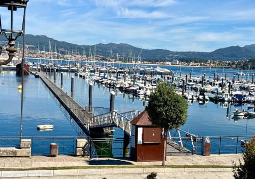 Marina con veleros y montañas costeras en el paseo marítimo de Baiona, España
